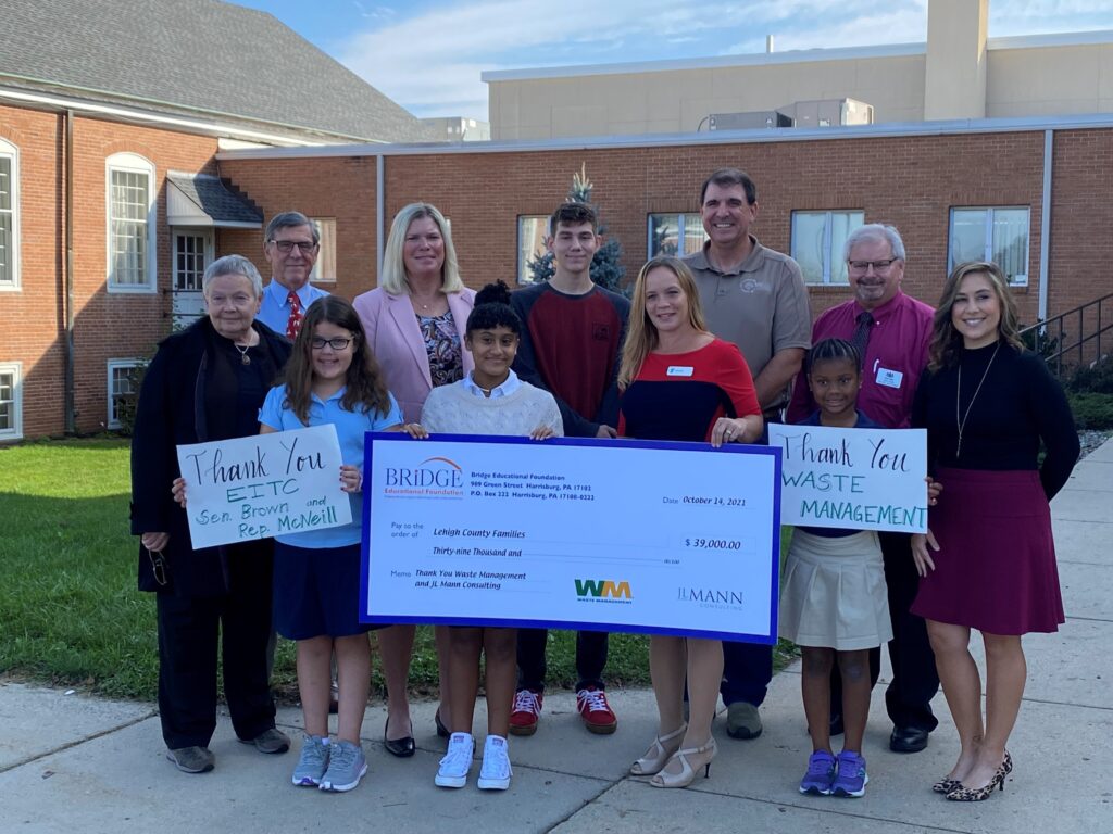 Representatives of Bridge Educational Foundation hold a mock check with students and GMS staff for scholarship assistance