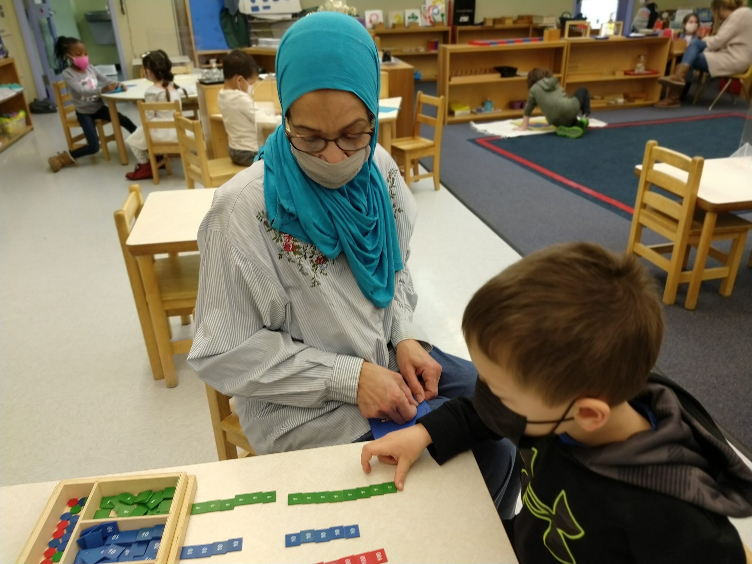 Mrs. Attia helps a student with a fun Montessori activity with green, blue, and red squares