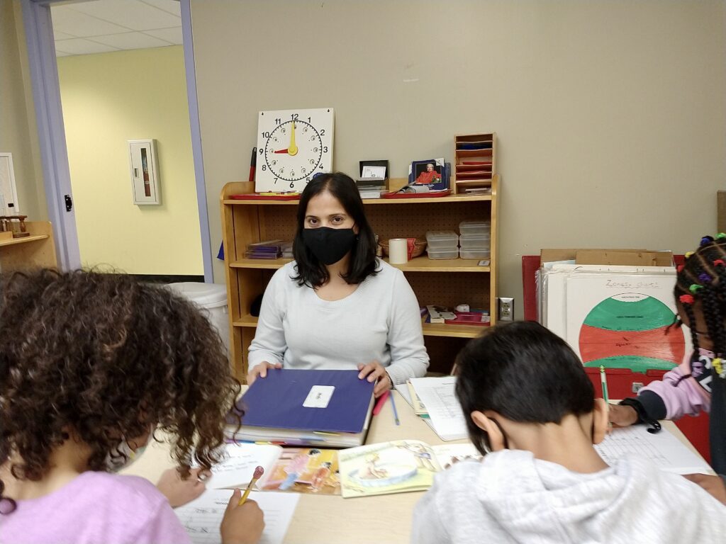 Ms. Radhika sits with students as they complete an activity