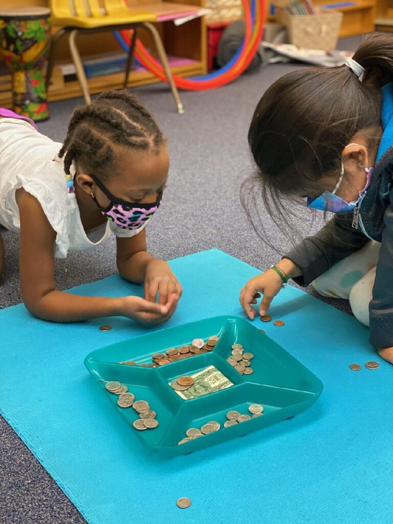 Two students sorting coins in a blue tray