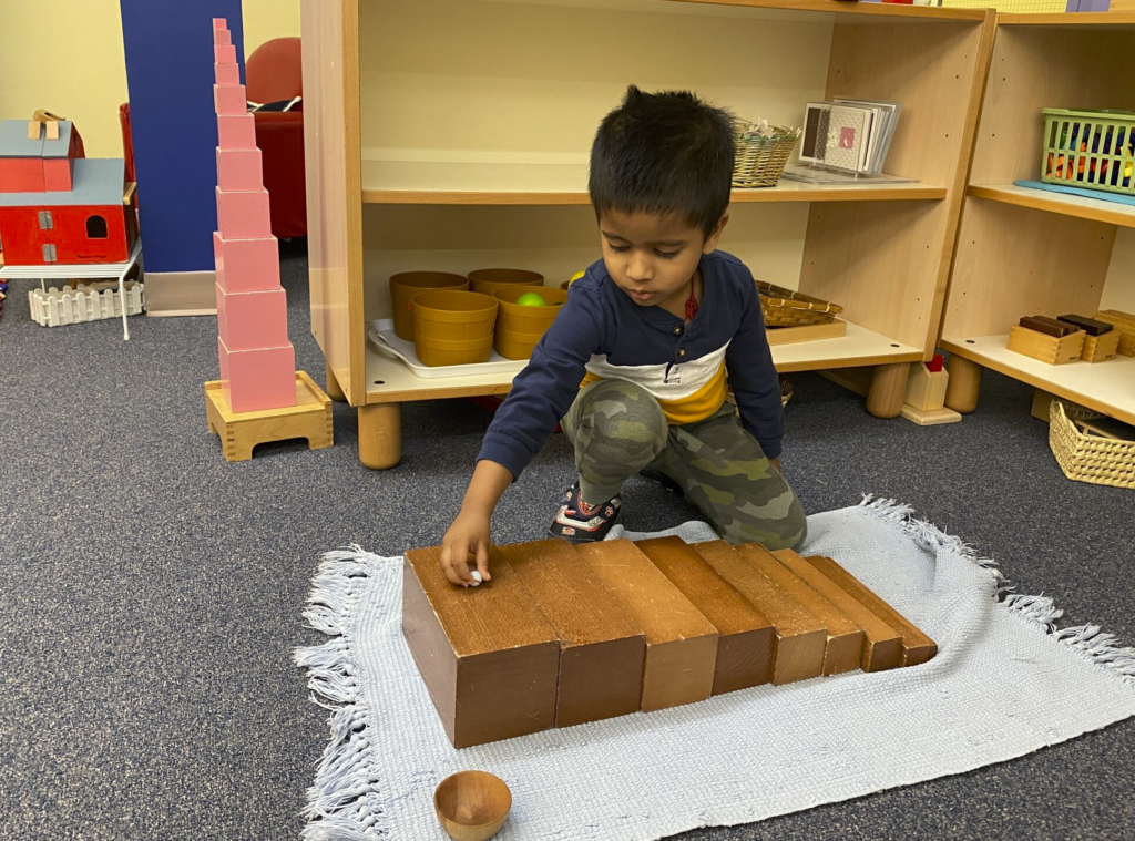 boy plays with wooden toy on white blanket