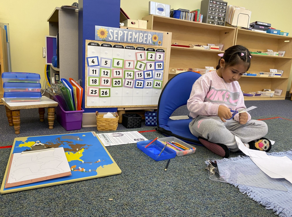 girl in pink shirt sits on floor with map of world in front of her